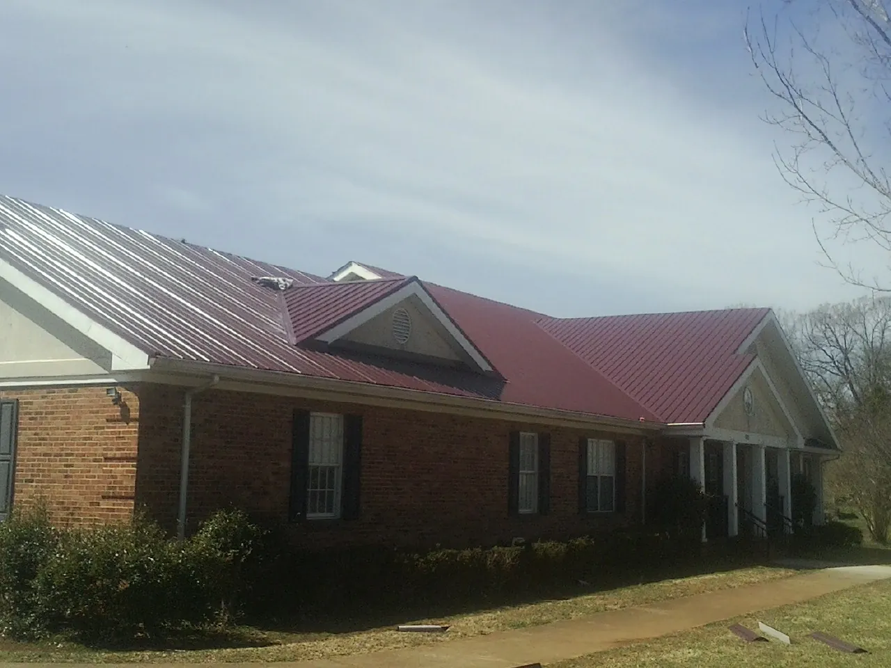 Red metal roof with gabled entries on a long brick building, from a Hail Damage Roof Repair job in Devers