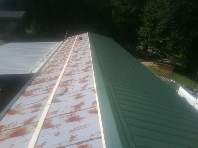Old rusted panels beside newly installed green metal roofing — Wind Damage Roof Repair by Roofing Brothers in Devers