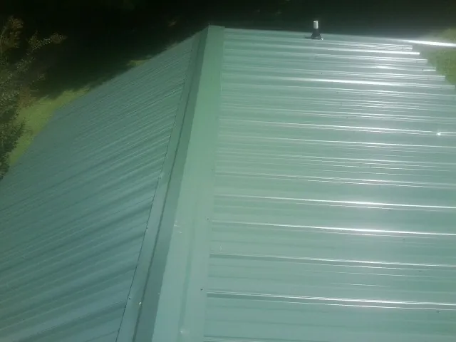 New green metal panels meeting at the ridge of a roof — Flat Roof Repair work by our crew in Devers