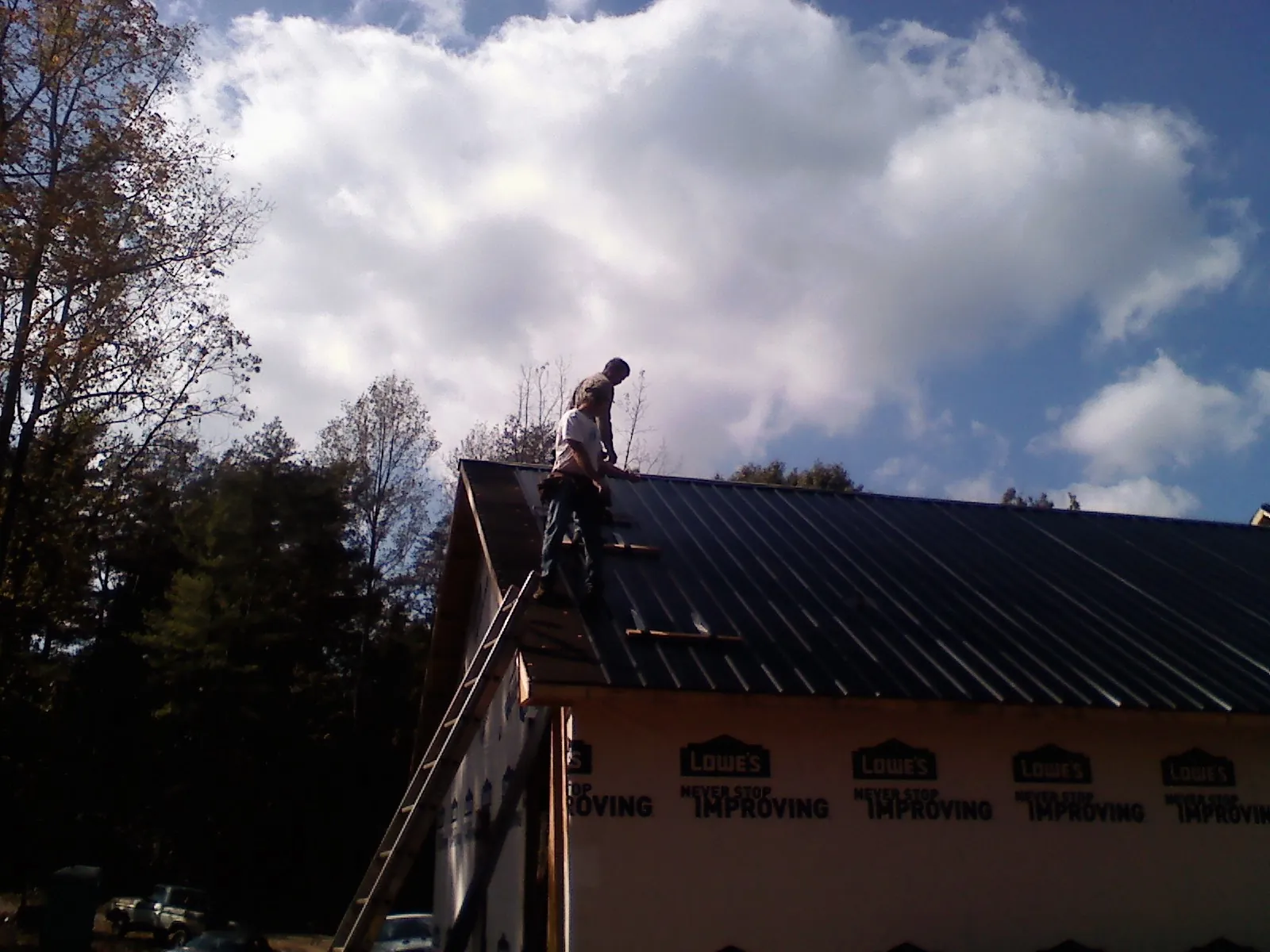 Roofer fastening dark metal panels high against a cloudy sky, from a Roof Inspection job in Devers