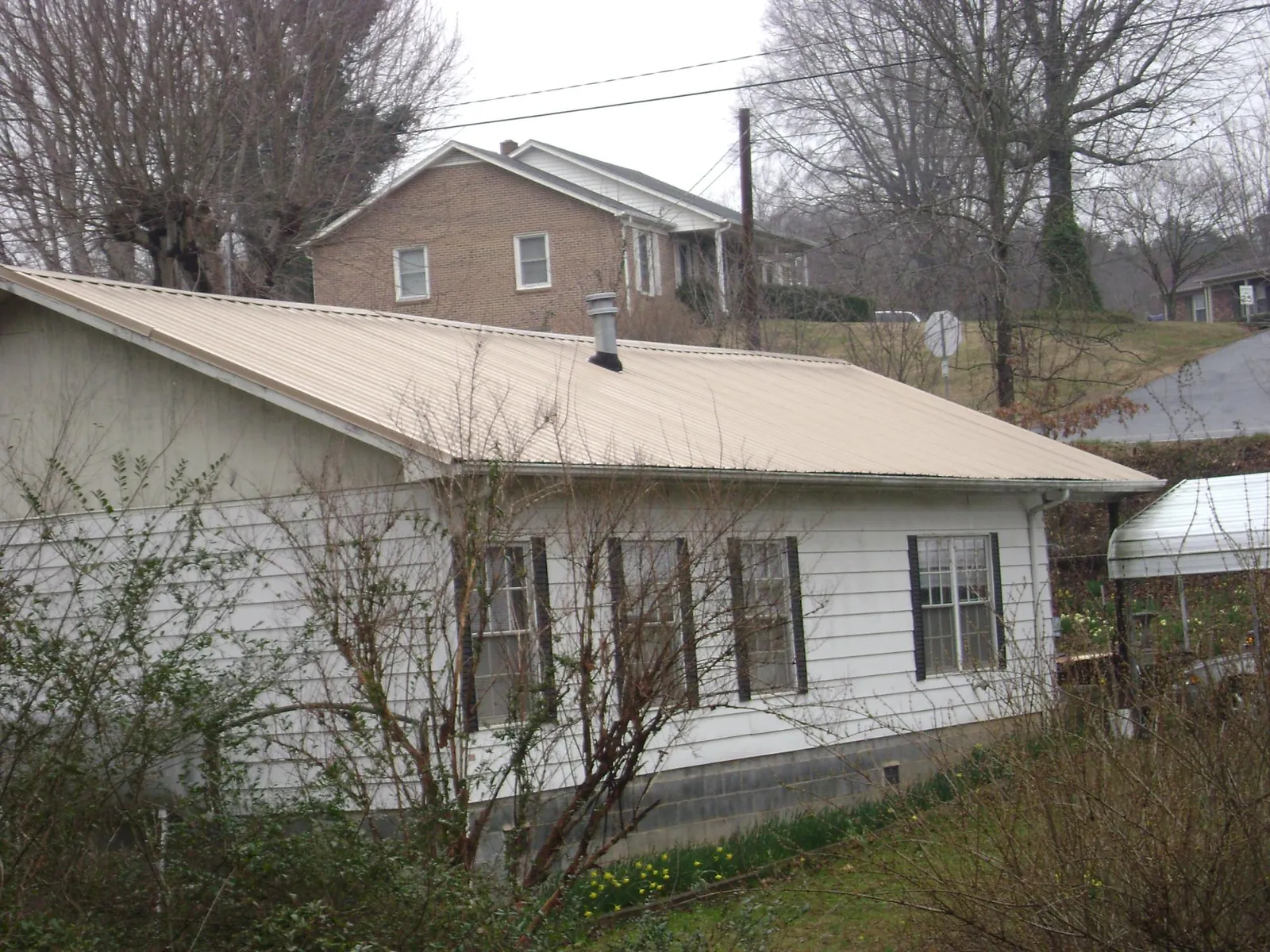 Tan metal roof on a white sided house set into a hillside — Commercial Roofing by Roofing Brothers in Devers