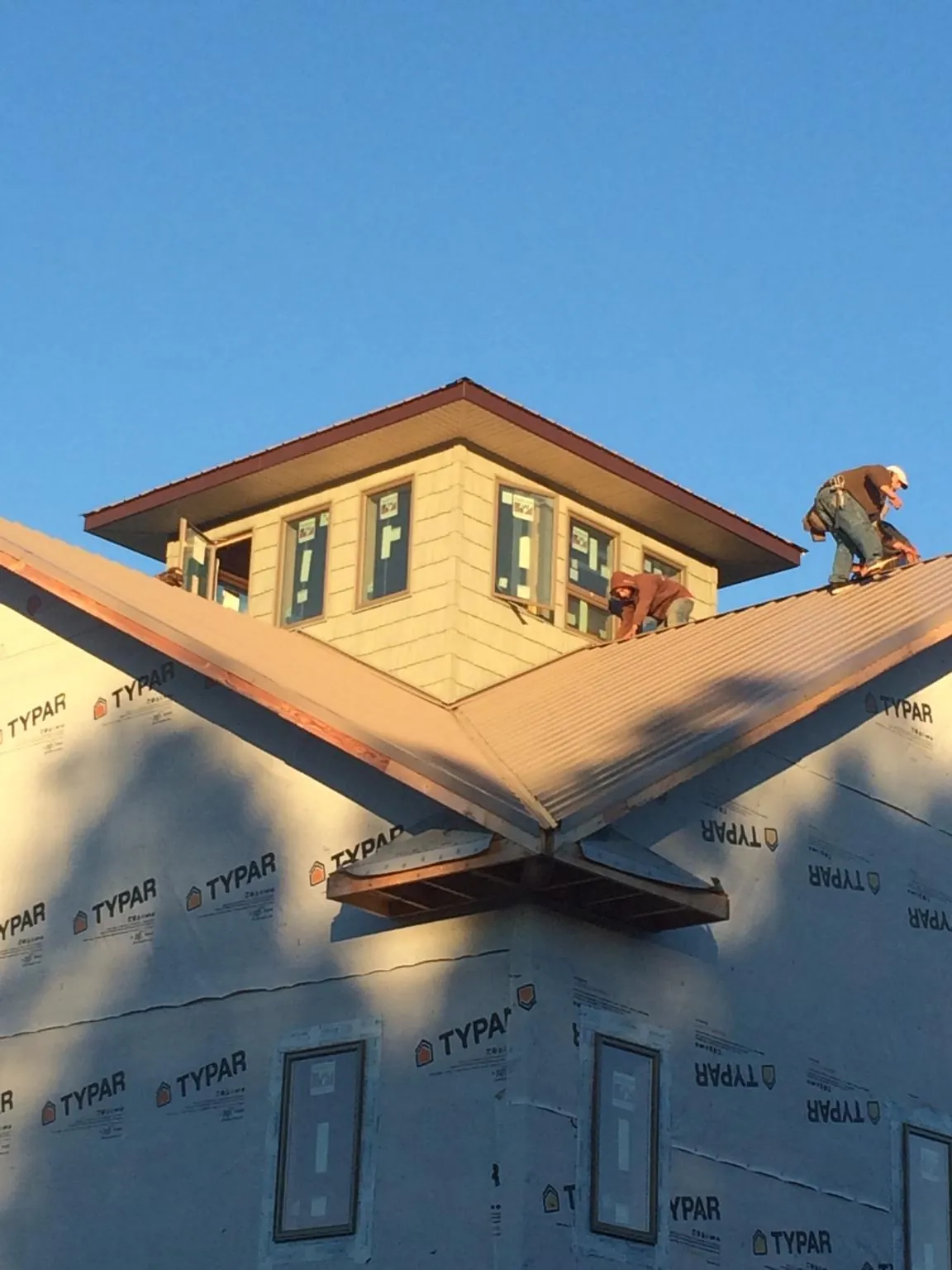 Roofers working around a rooftop cupola on a new metal roof at sunset — Roof Waterproofing in Devers by Roofing Brothers